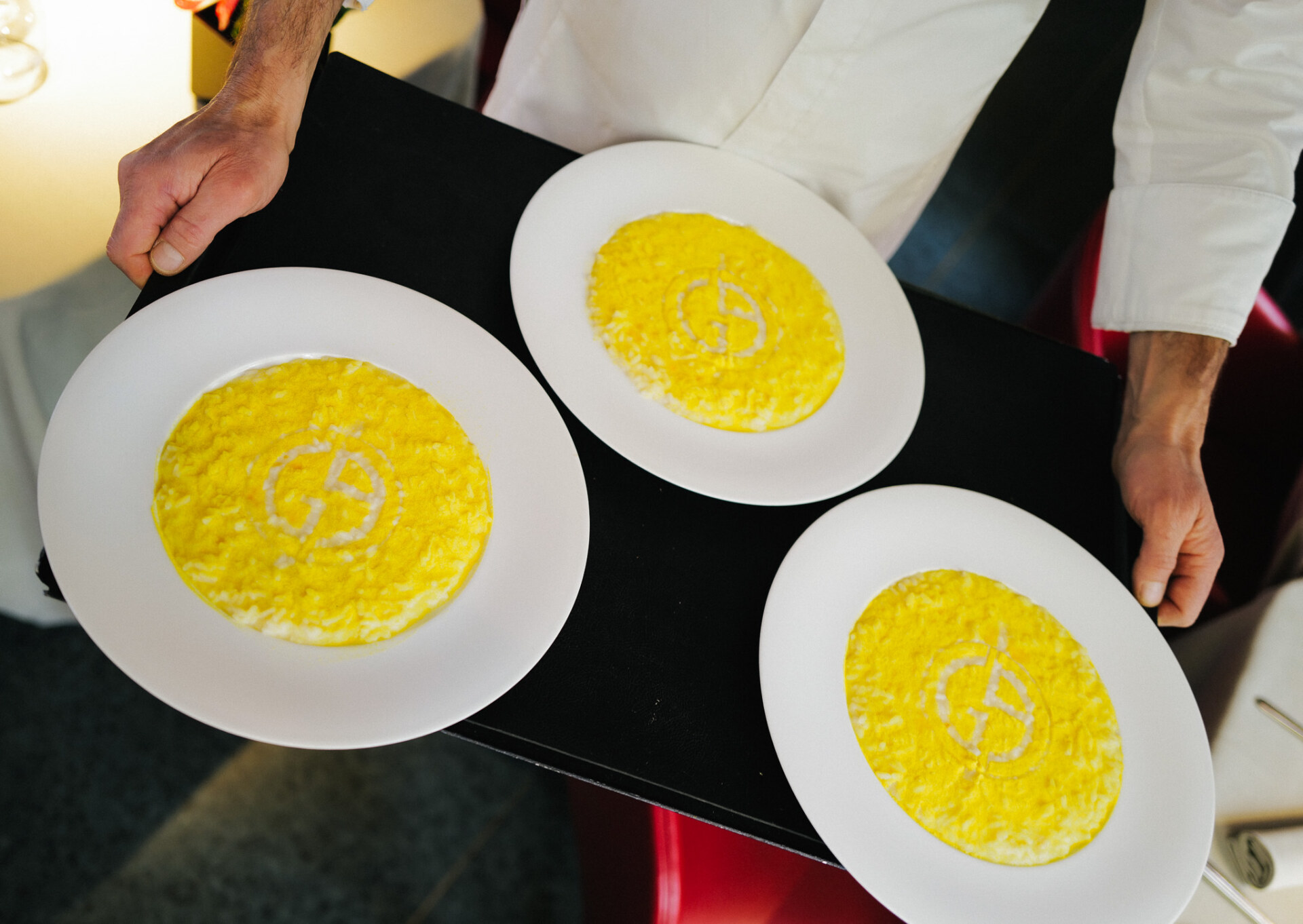 waiter holding tray of three bowls of safron risotto at armani restaurant milan