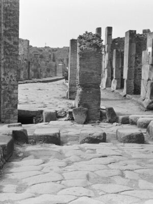a black and white image of pompeii in 1967 with a woman standing amidst ruins