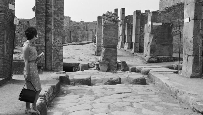 a black and white image of pompeii in 1967 with a woman standing amidst ruins