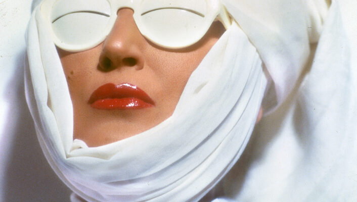 Moda futuristica - Persona con labbra rosse e un panno bianco avvolto intorno alla testa, che indossa occhiali da sole bianchi lucidi che coprono completamente gli occhi, creando un look futuristico.