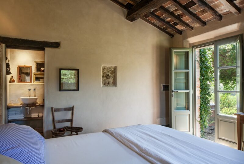 a room at Follonico looking out onto the green lush countryside with simple decor and a made bed