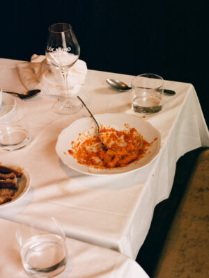 Localino - A dining table with a white cloth holds a plate of half-eaten pasta and several empty glasses, including a wine glass. There are also a few teaspoons scattered around the table. The scene suggests a recently finished meal.