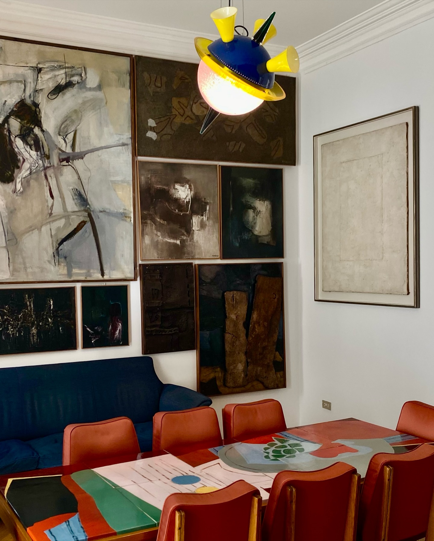 [Titolo dell'immagine] - Una stanza con arte astratta alle pareti, un divano blu e un tavolo colorato con sedie rosse. Un'esclusiva lampada a tema pianeta pende dal soffitto.