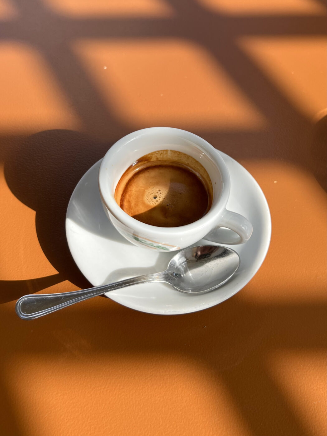 Nella tua descrizione non è specificato alcun titolo per l'immagine, ma se ce ne fosse uno, il formato da seguire sarebbe: "[Titolo immagine] - [Testo alternativo]". Poiché qui abbiamo solo i dettagli del testo alternativo, potresti descriverlo semplicemente come: "Una piccola tazza di espresso è appoggiata su un piattino bianco, accompagnata da un cucchiaino d'argento. Il set è appoggiato su un caldo tavolo marrone con ombre incrociate proiettate dai vetri delle finestre". Se hai un titolo per l'immagine che vorresti includere, forniscilo.