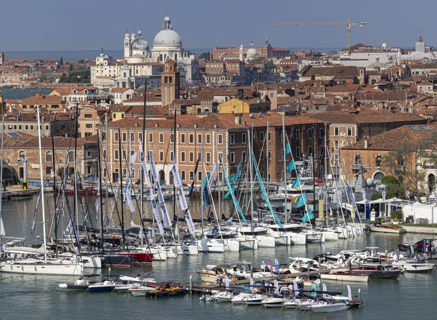 Venetian Marina - A view of a marina with numerous sailboats docked, set against a backdrop of historic Venetian architecture, including domed and terracotta-roofed buildings. The cityscape extends towards the horizon under a clear blue sky.