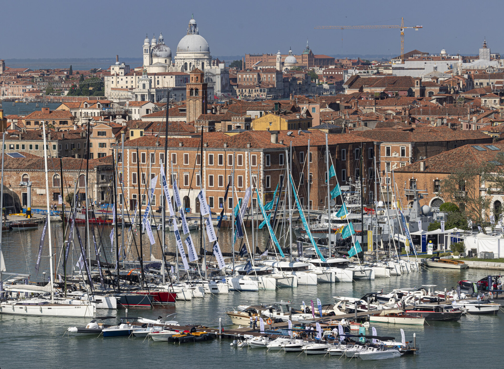 Venetian Marina - A view of a marina with numerous sailboats docked, set against a backdrop of historic Venetian architecture, including domed and terracotta-roofed buildings. The cityscape extends towards the horizon under a clear blue sky.