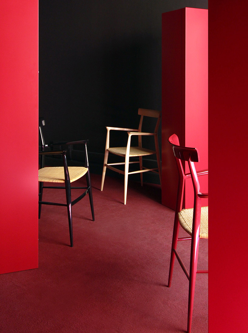 Three Modern Chairs in Minimalist Setting - A room with red walls and floor features three modern chairs with woven seats. Two chairs are red and black, while the third is natural wood. The setting is minimalist and stylish, with bold red partitions accentuating the space.