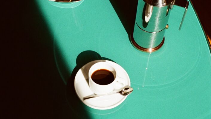 Conica Espresso Coffee Maker : Teal Table with Meringue Cookies and Espresso - A teal table with a bowl of meringue cookies, a silver coffee maker, and a cup of espresso on a saucer with a spoon. Strong sunlight casts dramatic shadows across the scene.