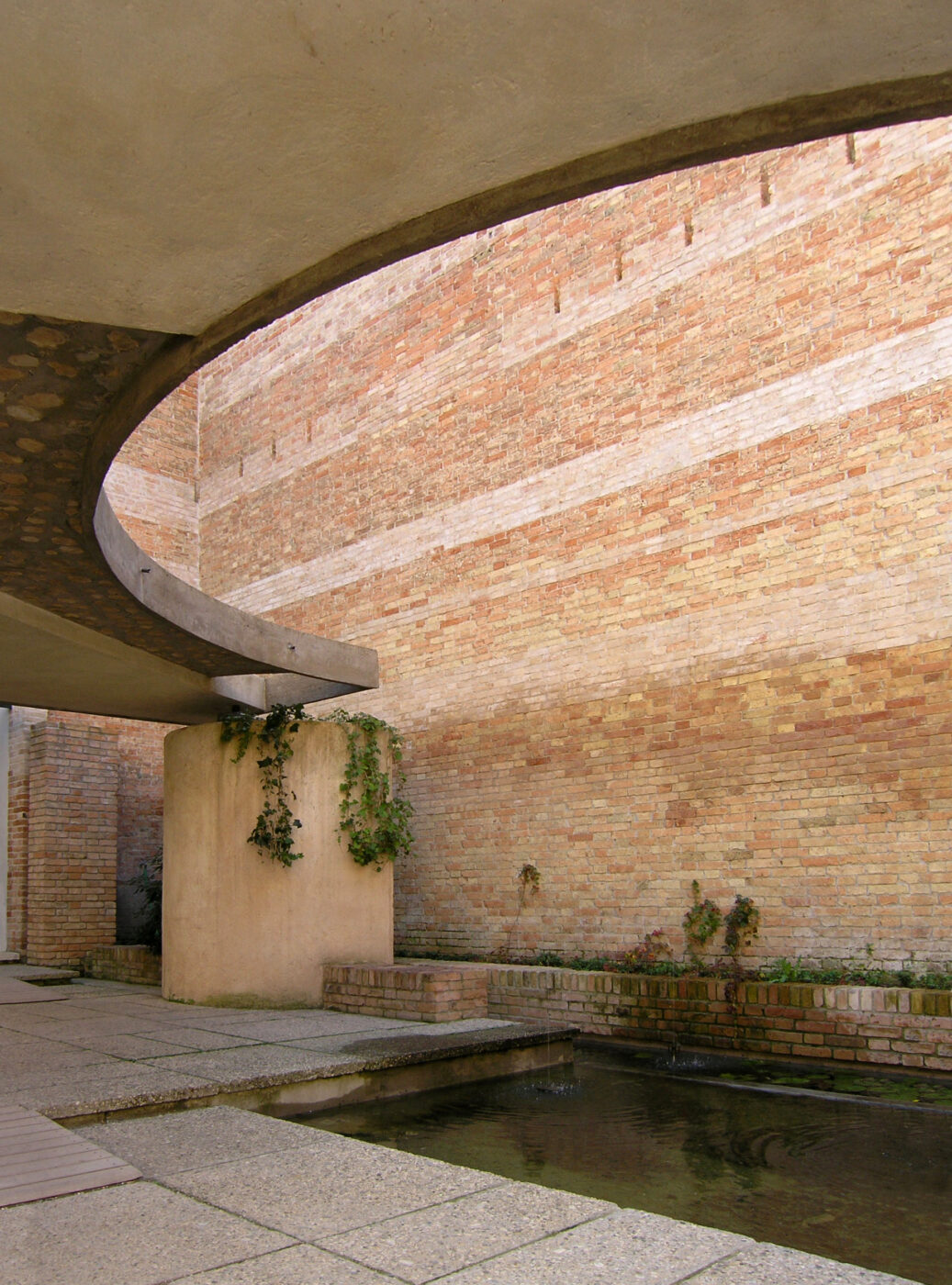 Modern Sanctuary - Uno spazio architettonico moderno con strutture curve in cemento, un muro di mattoni e una piccola fontana. Le piante rampicanti crescono su un pilastro di cemento, aggiungendo verde al design altrimenti minimalista.