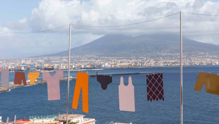 [Scenic Laundry Day] - Clothes hanging on a line with a scenic view of a bay and distant mountains. The garments sway gently, with a cityscape and fluffy clouds in the background under a clear blue sky.