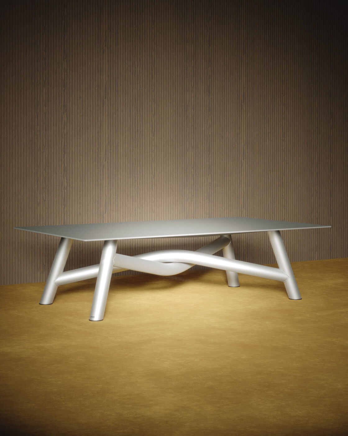 Partitina 0–6 Table - A modern table with a flat, dark gray surface and white, curved legs, set against a textured beige backdrop and gold flooring. The design is minimalist with a sculptural, intertwined base.