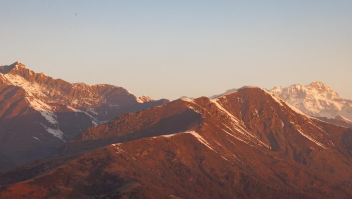 Mountain range at sunset - Mountain range at sunset with warm light illuminating the peaks, some of which are dusted with snow, under a clear sky.