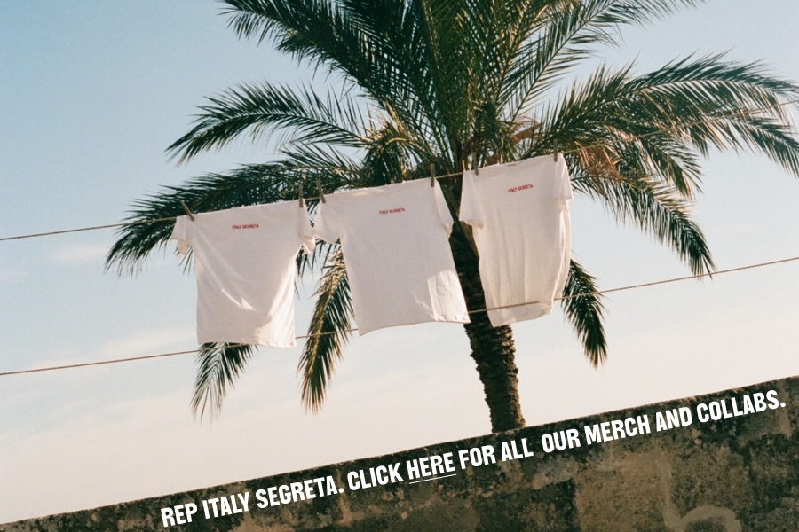 REP ITALY SEGRETA - Due magliette bianche sono appese a uno stendibiancheria davanti a una palma, sotto un cielo limpido. In basso c'è la scritta: REP ITALY SEGRETA. CLICCA QUI PER TUTTO IL NOSTRO MERCHANDISE E LE NOSTRE COLLABORAZIONI.