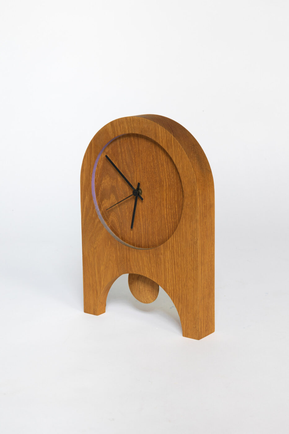 Orologio in legno - Un orologio in legno con la parte superiore arrotondata e due gambe, con lancette nere per le ore e i minuti. Il quadrante è incastonato nel legno e il design è minimalista e moderno. Lo sfondo è bianco.