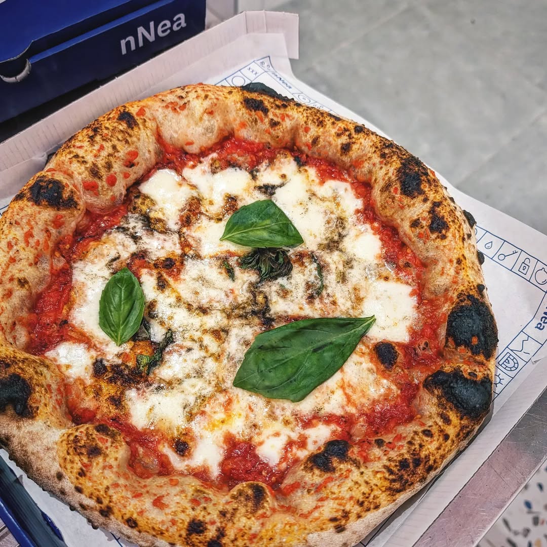 Neapolitan pizza in Amsterdam - A freshly baked Neapolitan pizza topped with melted mozzarella cheese, tomato sauce, three basil leaves, and slightly charred bubbly crust, placed on a paper-lined box.