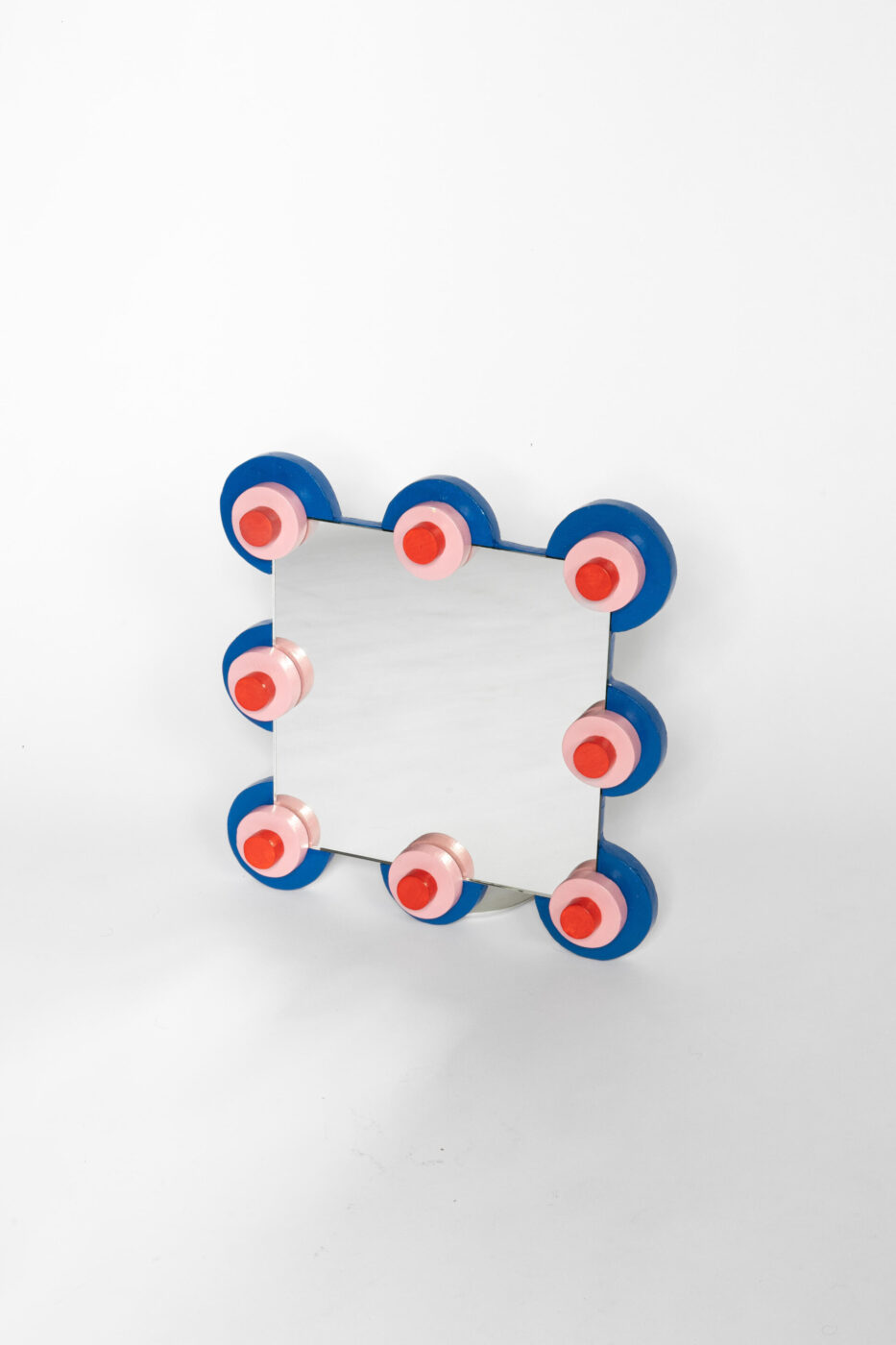 Specchio rettangolare con otto pomelli circolari: uno specchio rettangolare con otto pomelli circolari, ciascuno blu con centro rosa e rosso, posizionati lungo i bordi su uno sfondo bianco.
