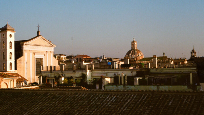 A cityscape at sunset - A cityscape at sunset shows historic buildings with domes and rooftops bathed in golden light under a clear blue sky.
