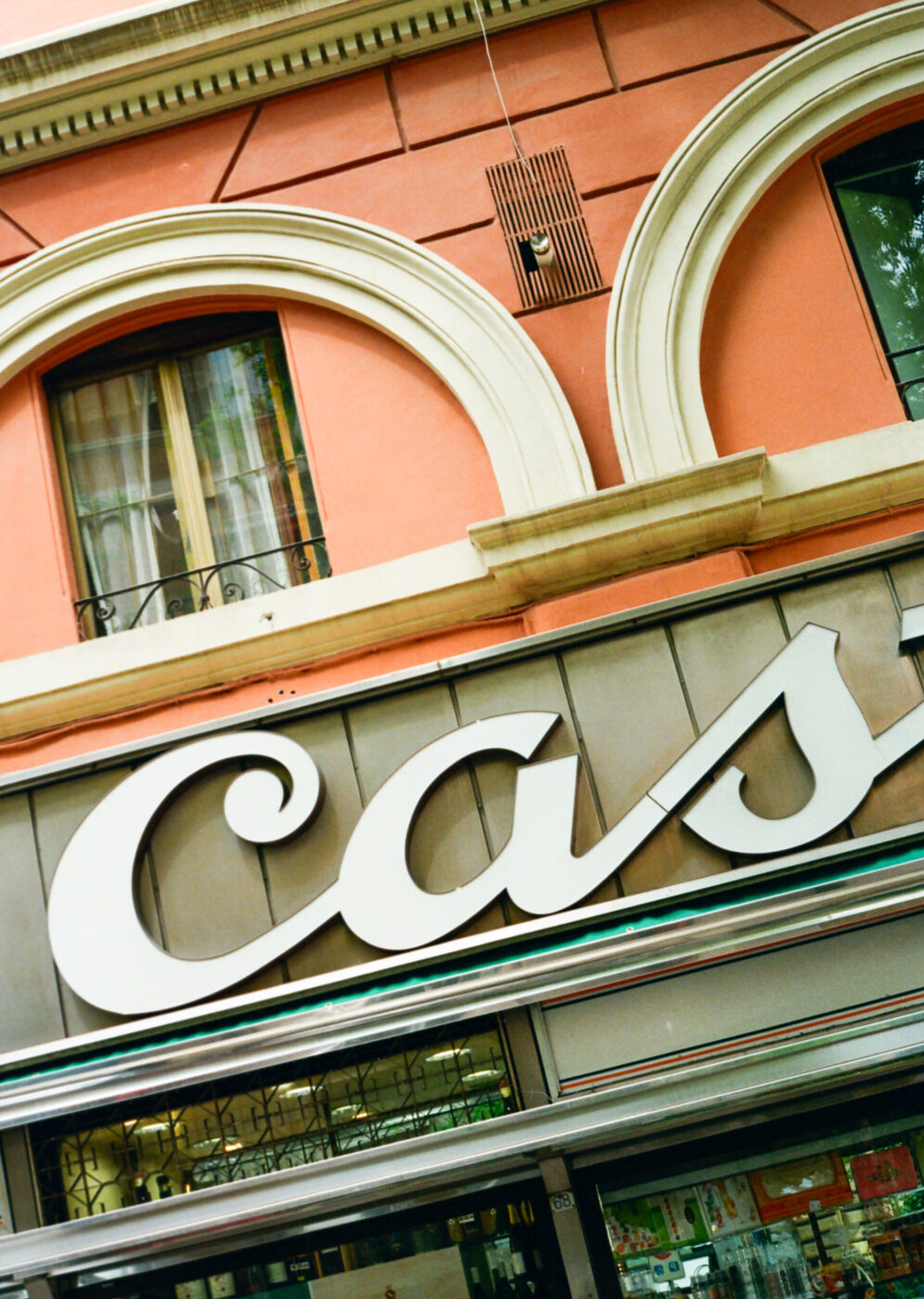 Insegna di un negozio CAS: primo piano della facciata di un edificio con finestre ad arco sopra un'insegna di un negozio che mostra grandi lettere bianche parzialmente visibili, C A S, su una parete color pesca.