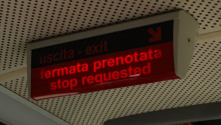 Uscita - exit / fermata prenotata - stop requested - A digital sign inside a vehicle displays “uscita - exit” and “fermata prenotata - stop requested” in red letters, indicating a passenger has requested the next stop.
