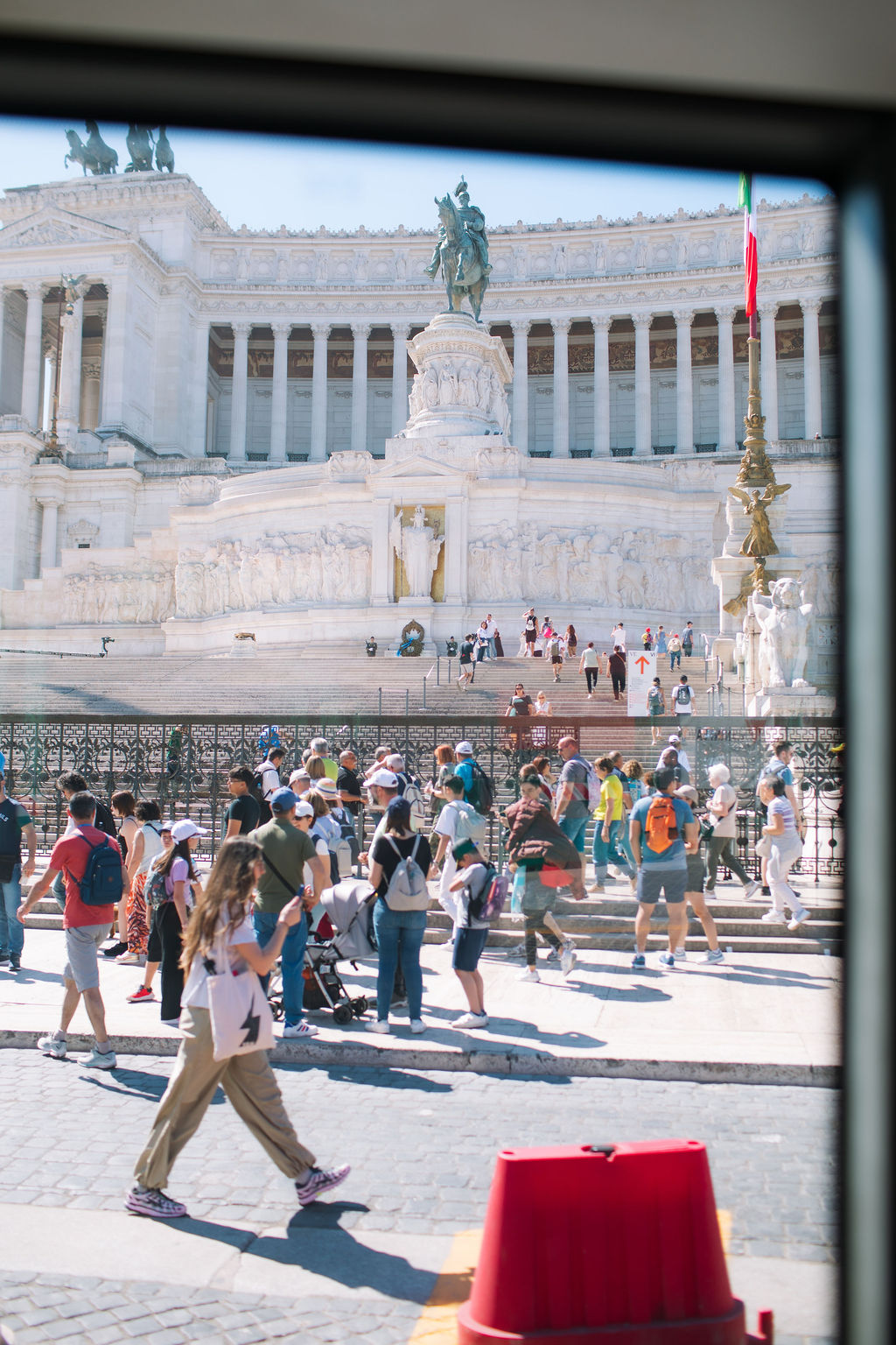 Vittoriano monument in Rome - A crowd of tourists walks and gathers in front of the large white marble Vittoriano monument in Rome, Italy, with statues, columns, and an Italian flag visible in the background.
