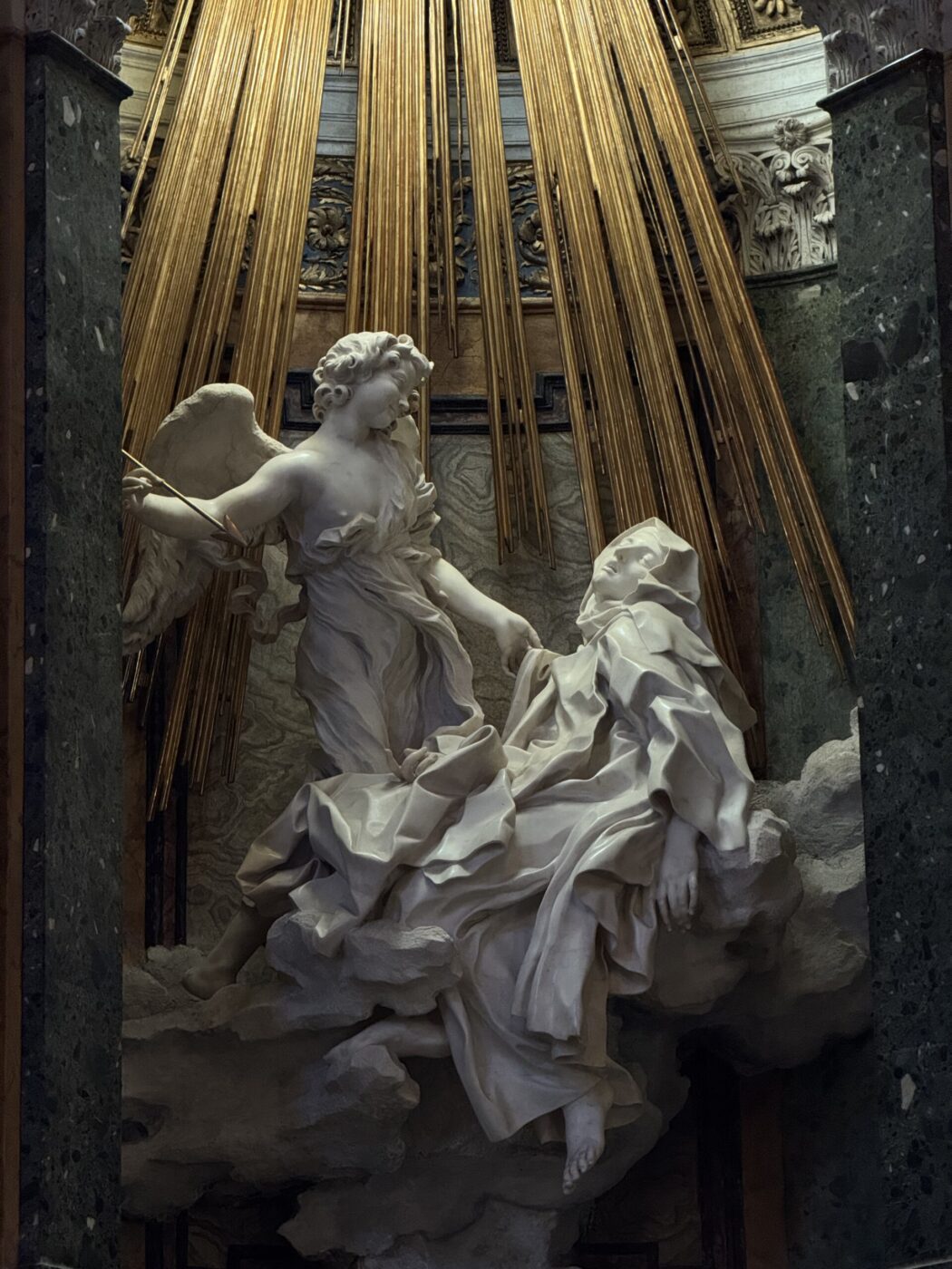 L'Estasi di Santa Teresa - Scultura barocca in marmo raffigurante un angelo e una donna sdraiata, circondati da raggi dorati, su uno sfondo drammatico con nuvole; probabilmente raffigura una scena religiosa o spirituale.