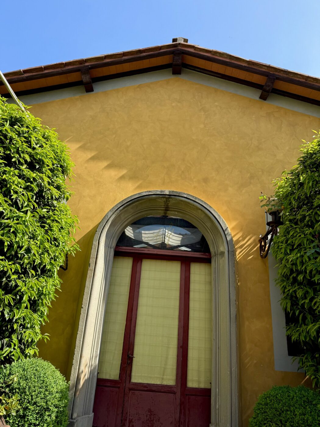 Certo! Ecco come scriveresti il testo alternativo se è presente un titolo immagine: Se il titolo dell'immagine è "Sunny Villa", il testo alternativo dovrebbe essere: Sunny Villa - Un edificio in stucco giallo con una porta ad arco con cornice rossa e pannelli in vetro, circondato da cespugli e alberi verdi, sotto un cielo azzurro e terso. Se non c'è un titolo, usa semplicemente: Un edificio in stucco giallo con una porta ad arco con cornice rossa e pannelli in vetro, circondato da cespugli e alberi verdi, sotto un cielo azzurro e terso.
