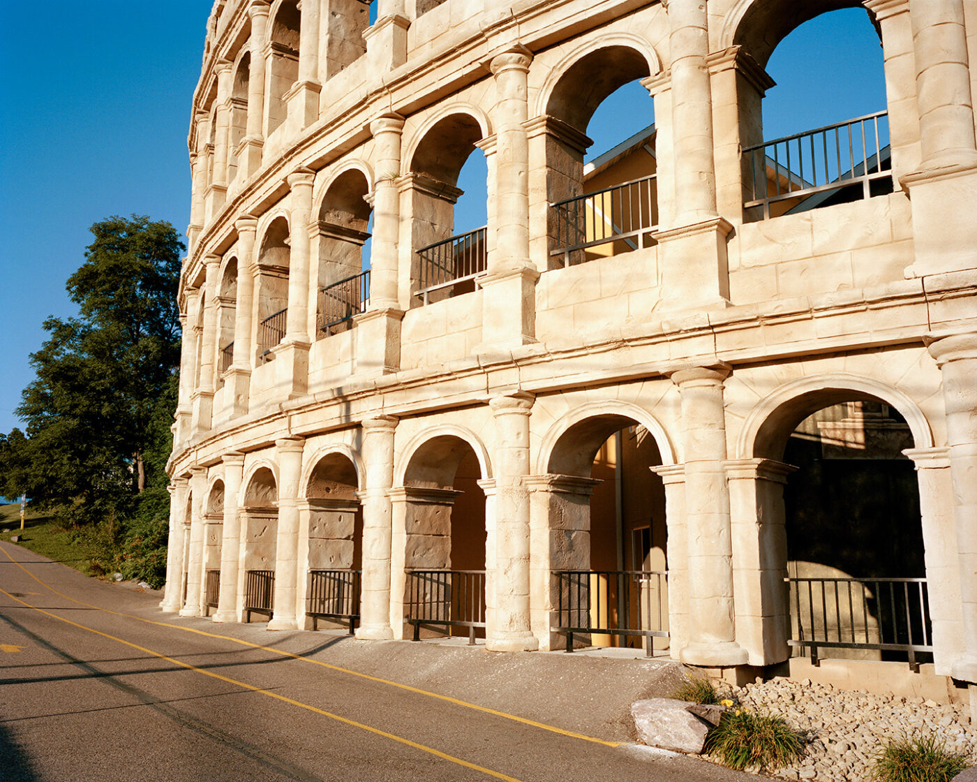 Roman Amphitheater - A partial view of a large stone building resembling the Roman Colosseum, with multiple arches and columns, next to a paved road under a clear blue sky. If no image title is available, you would use just: A partial view of a large stone building resembling the Roman Colosseum, with multiple arches and columns, next to a paved road under a clear blue sky. Would you like me to create more examples or assist in formatting other descriptions?.