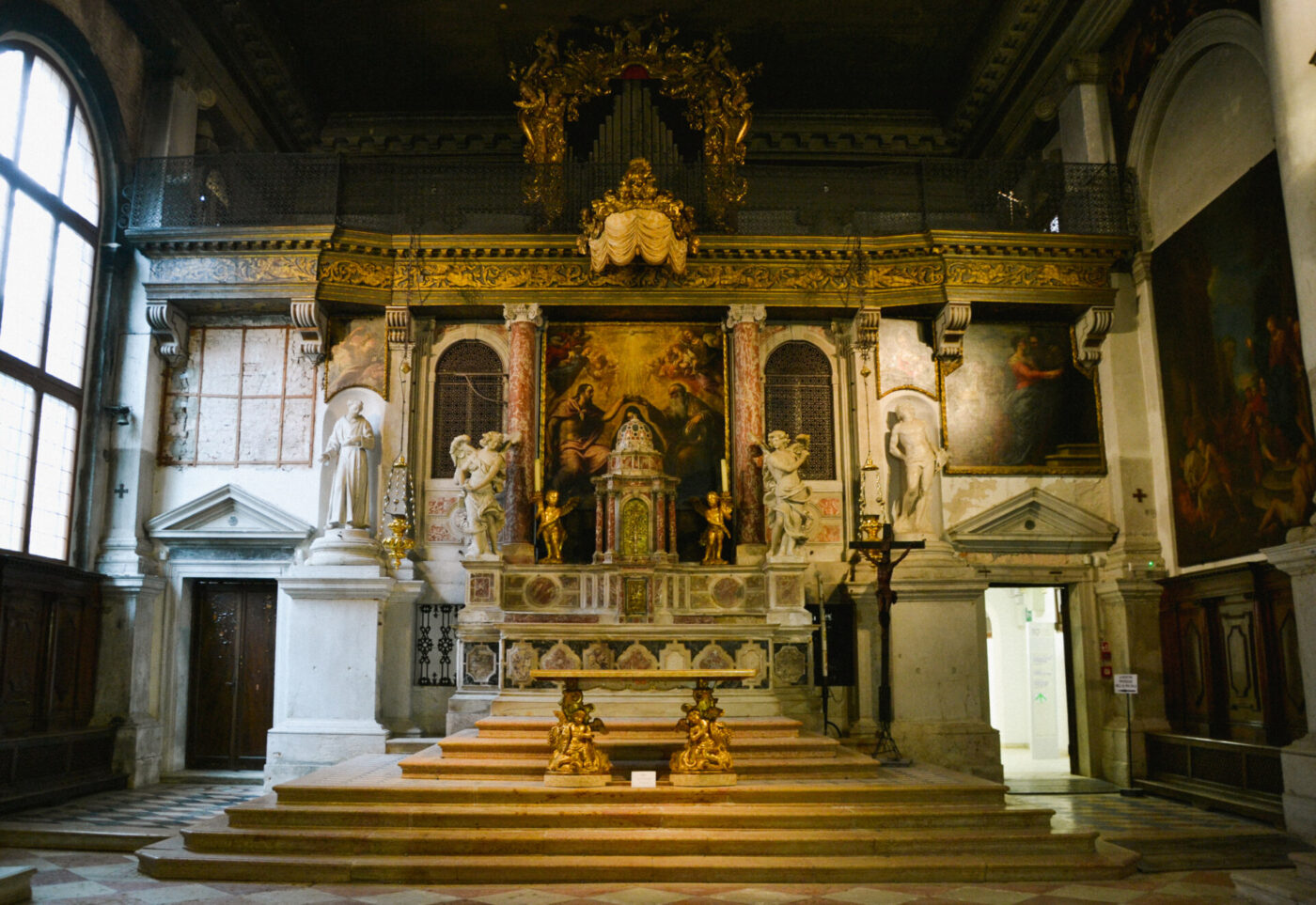 Altare decorato della chiesa - Altare decorato della chiesa con accenti dorati, statue di angeli, grandi dipinti religiosi e gradini in marmo, situato in un grande interno storico con alte finestre e intricati dettagli architettonici.