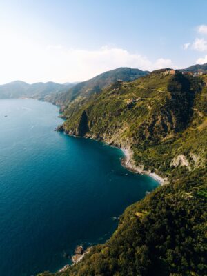 Vista aerea di una costa frastagliata con ripide colline verdeggianti che incontrano il mare blu intenso sotto un cielo limpido. Piccole insenature e scogliere costeggiano l'acqua e il paesaggio si estende a perdita d'occhio. *Se fornisci il titolo dell'immagine, lo includerò all'inizio secondo le tue istruzioni.*.