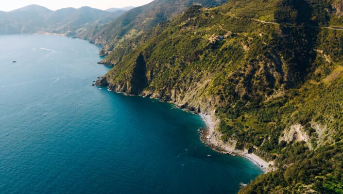 Vista aerea di una costa frastagliata con ripide colline verdeggianti che incontrano il mare blu intenso sotto un cielo limpido. Piccole insenature e scogliere costeggiano l'acqua e il paesaggio si estende a perdita d'occhio. *Se fornisci il titolo dell'immagine, lo includerò all'inizio secondo le tue istruzioni.*.