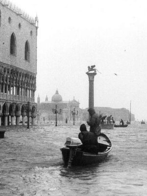 St. Mark’s Square Flooding - A black-and-white photo of people in a small boat navigating a heavily flooded St. Mark’s Square in Venice, Italy. Historic buildings and columns are partially submerged under high water.
