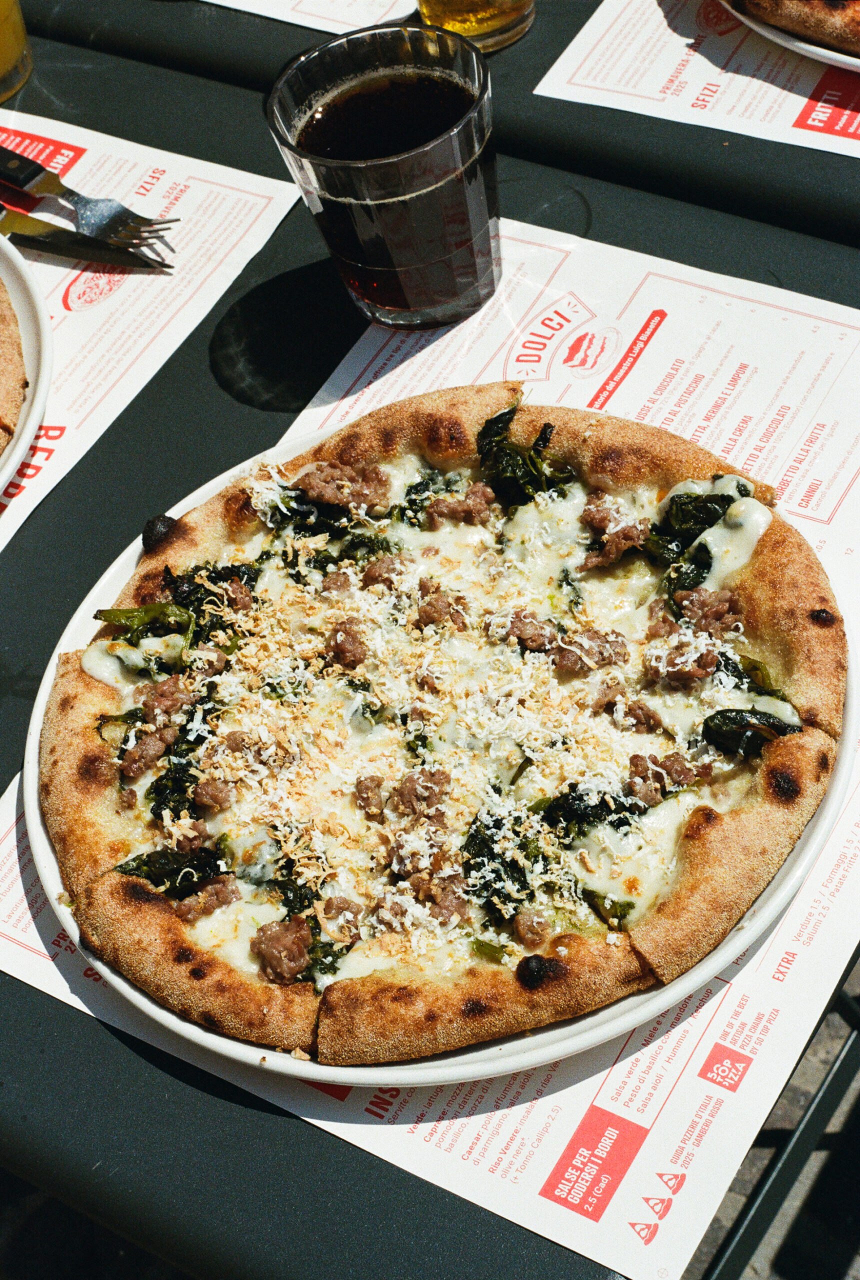 A pizza on a sunlit table topped with sausage and friarielli