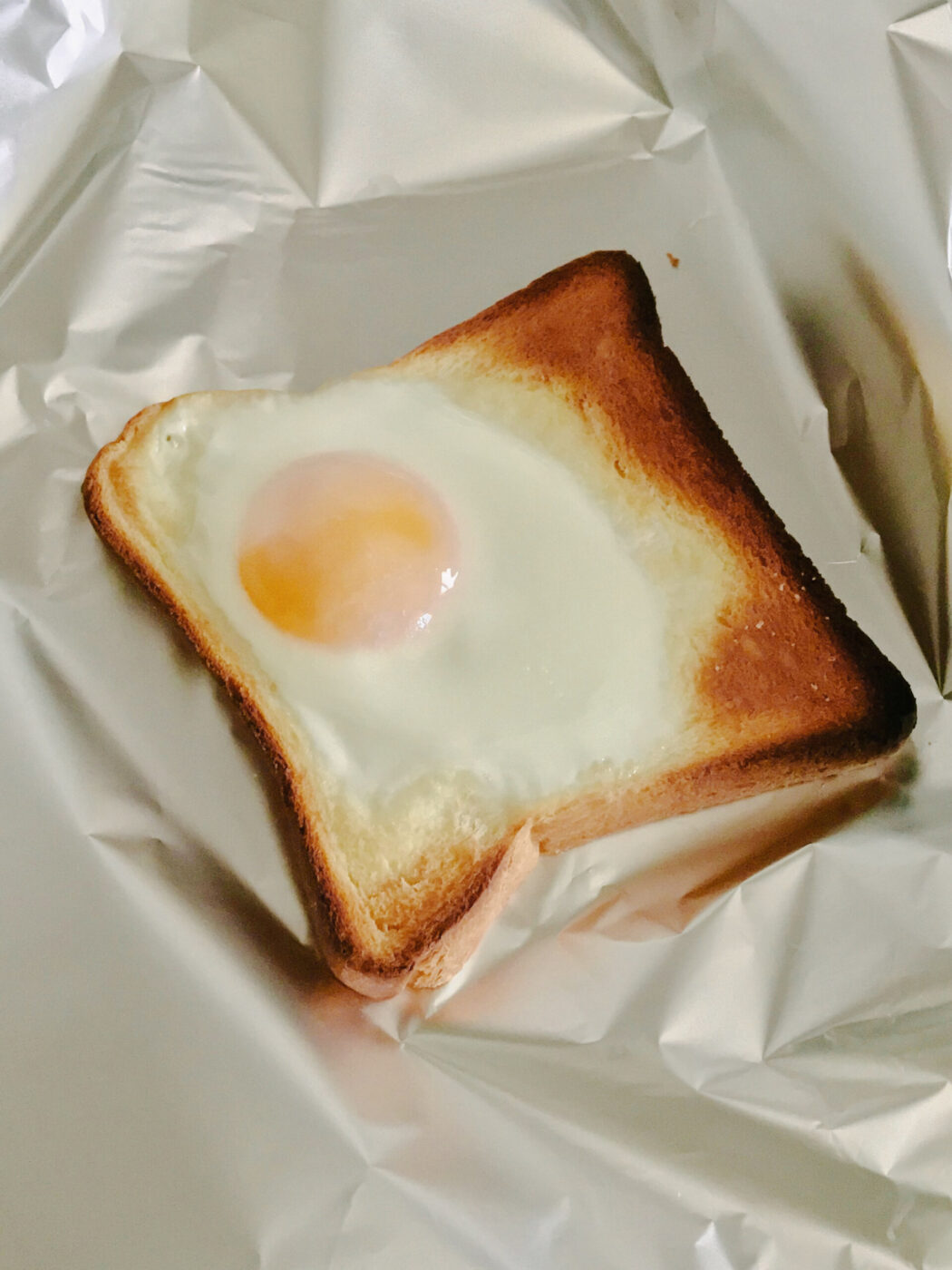[Nessun titolo dell'immagine] - Una fetta di pane tostato con un uovo cotto al centro è adagiata su un foglio di alluminio stropicciato.