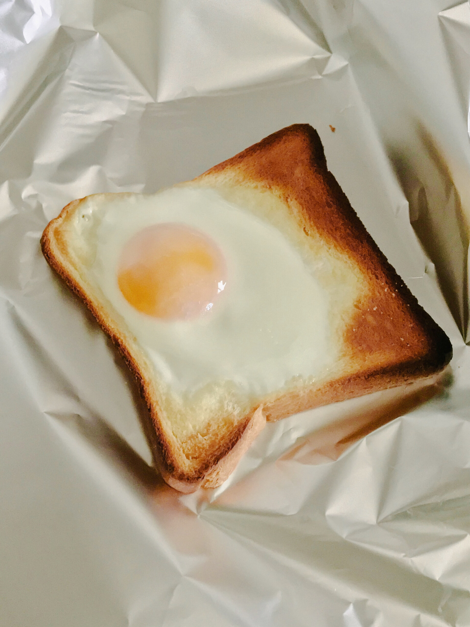 [Nessun titolo dell'immagine] - Una fetta di pane tostato con un uovo cotto al centro è adagiata su un foglio di alluminio stropicciato.