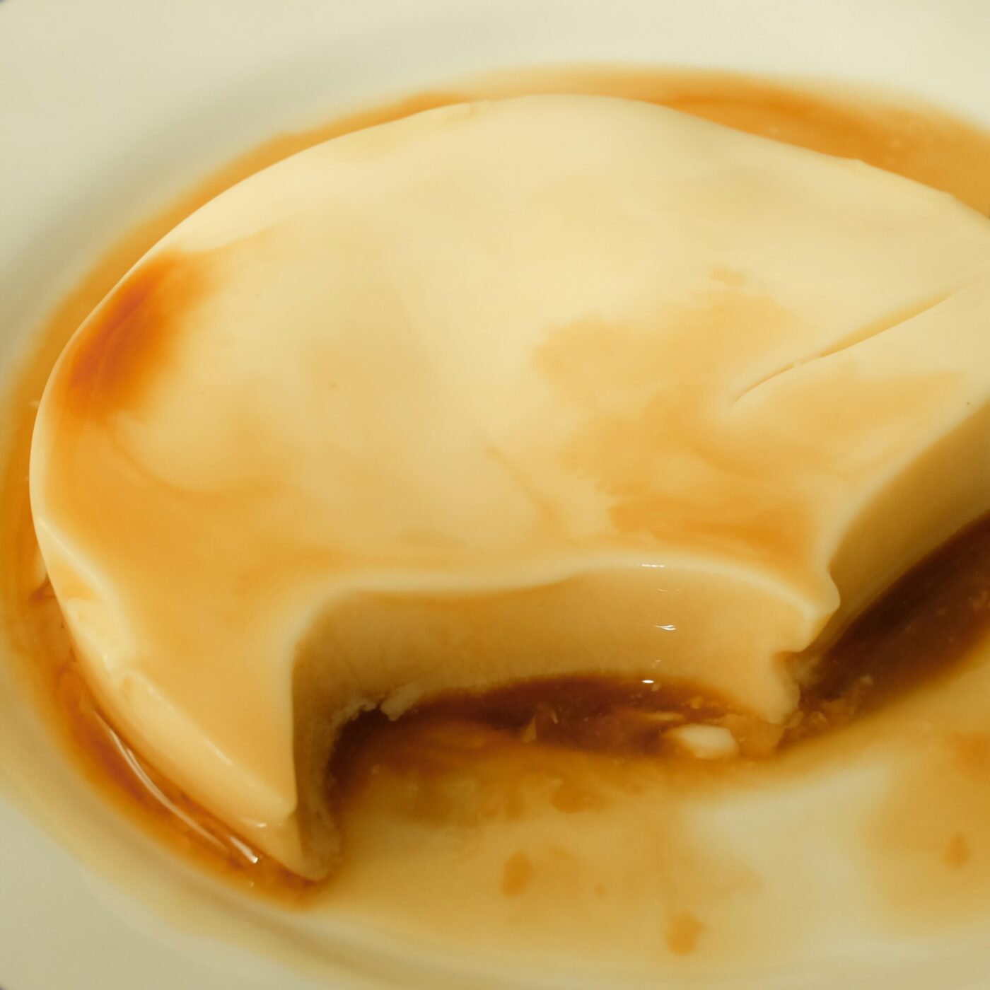 Un cremoso flan con salsa al caramello - Un cremoso flan con salsa al caramello, servito su un piatto bianco. Un pezzo è stato estratto, rivelando la consistenza morbida dell'interno.