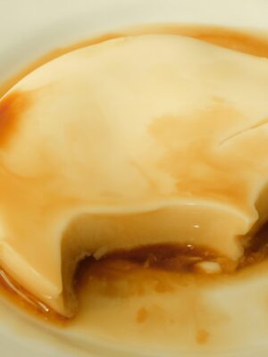 Un cremoso flan con salsa al caramello - Un cremoso flan con salsa al caramello, servito su un piatto bianco. Un pezzo è stato estratto, rivelando la consistenza morbida dell'interno.