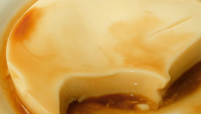 A creamy flan dessert with caramel sauce - A creamy flan dessert with caramel sauce sits on a white plate. A large bite has been taken from the flan, revealing its smooth texture and light brown color inside.