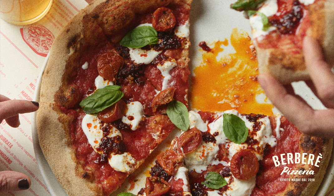 BERBERÈ Pizzeria - A close-up of a pizza topped with tomato sauce, mozzarella, cherry tomatoes, basil leaves, and chili oil on a plate. Two hands are reaching for slices. The text BERBERÈ Pizzeria is visible in the corner.