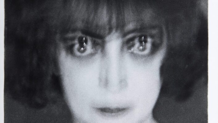 Portrait of: Luisa Casati Stampa A black and white blurry photo of a woman with shoulder-length hair and bangs, appearing to have two sets of eyes due to a double exposure effect. She looks directly at the camera with a blank expression.