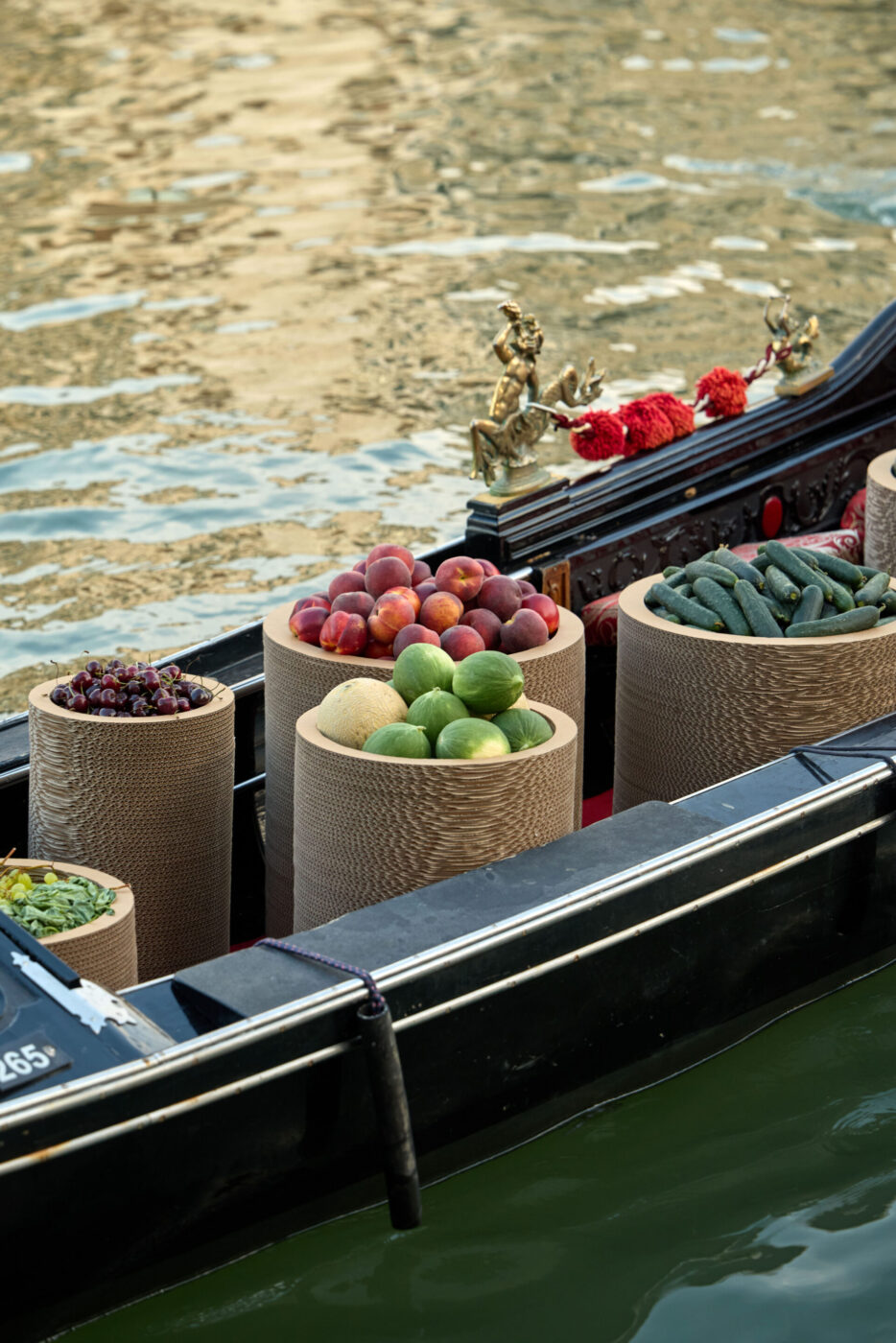 Una gondola piena di cesti di frutta e verdura fresca - Una gondola piena di cesti di pesche, zucchine, lime e altri prodotti galleggia sull'acqua calma. Statuette dorate e fiori rossi decorano il bordo della barca.