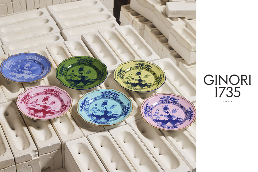 GINORI 1735 ITALIA - Cinque piatti ornati in rosa, verde, giallo, blu e viola con disegni floreali blu sono esposti su stampi in ceramica bianca. Il testo "GINORI 1735 ITALIA" compare sul lato destro dell'immagine.