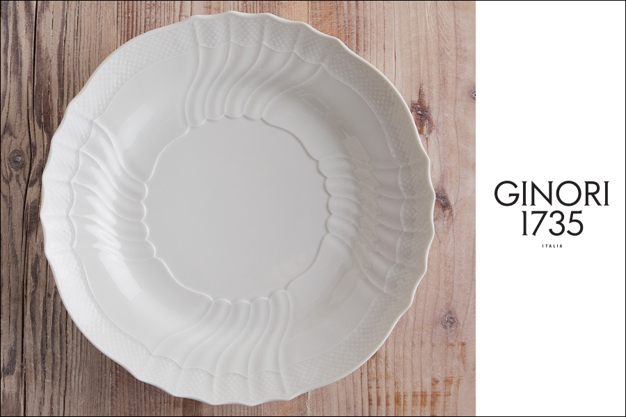 Certo! Ecco il testo alt seguendo le tue istruzioni: "GINORI 1735 ITALIA - Un piatto Ginori 1735 bianco, con motivi intricati, si trova su una superficie di legno, con il marchio GINORI 1735 ITALIA visualizzato in testo nero su sfondo bianco a destra.