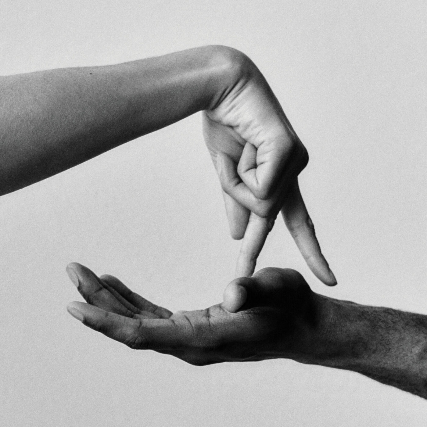 A black and white photo shows one hand held palm up while another hand, above it, points two fingers downward as if touching or walking on the palm. The background is plain and light-colored. If you have an image title, please provide it so I can format the alt text accordingly.