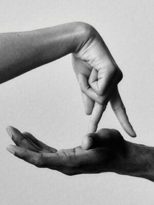 A black and white photo shows one hand held palm up while another hand, above it, points two fingers downward as if touching or walking on the palm. The background is plain and light-colored. If you have an image title, please provide it so I can format the alt text accordingly.