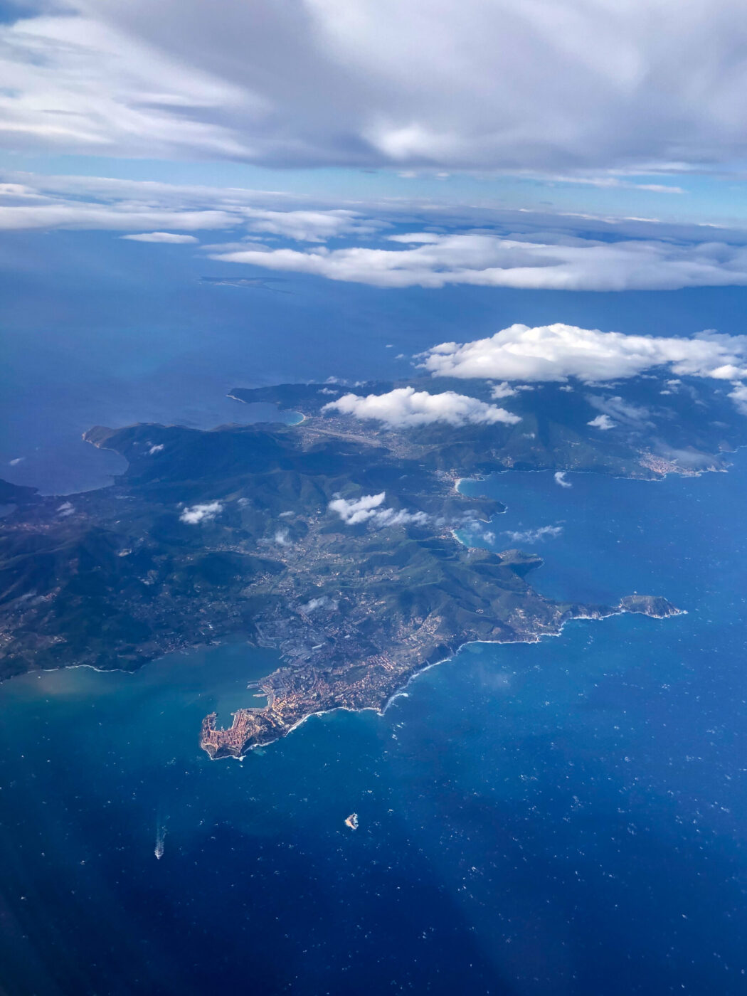 Veduta aerea di un paesaggio costiero con una penisola che si protende nel mare blu - Veduta aerea di un paesaggio costiero con una penisola che si protende in acque blu vibranti, parzialmente oscurata dalle nuvole; sono visibili le catene montuose, le piccole città lungo la costa e l'oceano circostante sotto un cielo per lo più nuvoloso.