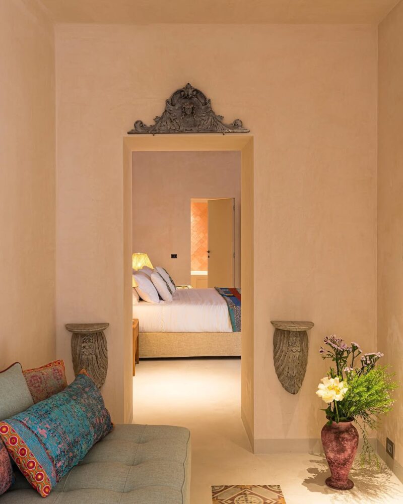 You havent specified an image title. If there is one, please provide it so I can format the alt text accordingly. If there is no image title, here’s the formatted alt text without it: A cozy, softly-lit room with a cushioned bench and colorful pillows leads to a bedroom with a bed, white bedding, and a lit lamp. Decorative wall accents and a vase of flowers add warmth and charm. If the image title is e.g. Inviting Home Interior, then per your instructions: Inviting Home Interior - A cozy, softly-lit room with a cushioned bench and colorful pillows leads to a bedroom with a bed, white bedding, and a lit lamp. Decorative wall accents and a vase of flowers add warmth and charm. Let me know if you’d like this tailored for any specific image title!.