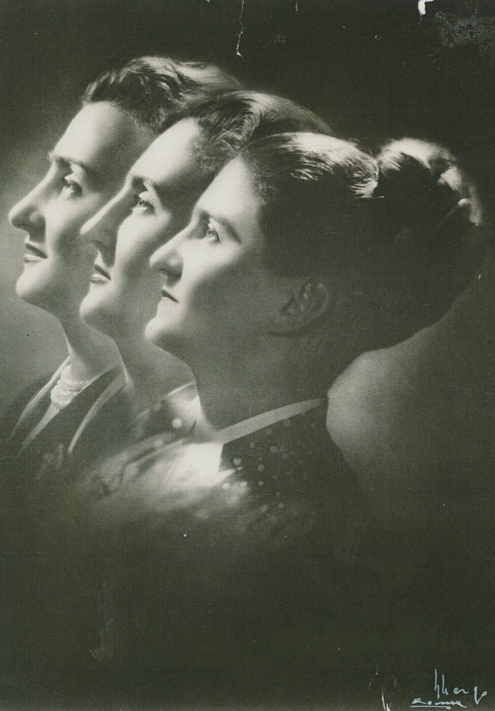 Tre donne di profilo, rivolte a sinistra, in piedi in diagonale, ognuna con capelli acconciati e abiti formali in una foto vintage in bianco e nero.