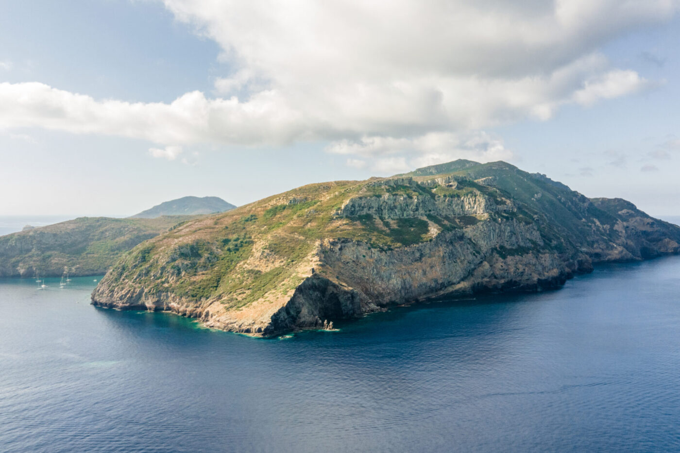 Veduta aerea di una grande isola rocciosa con vegetazione verde - Veduta aerea di una grande isola rocciosa ricoperta da una vegetazione verde e lussureggiante, circondata da acque oceaniche di un blu intenso, sotto un cielo parzialmente nuvoloso.