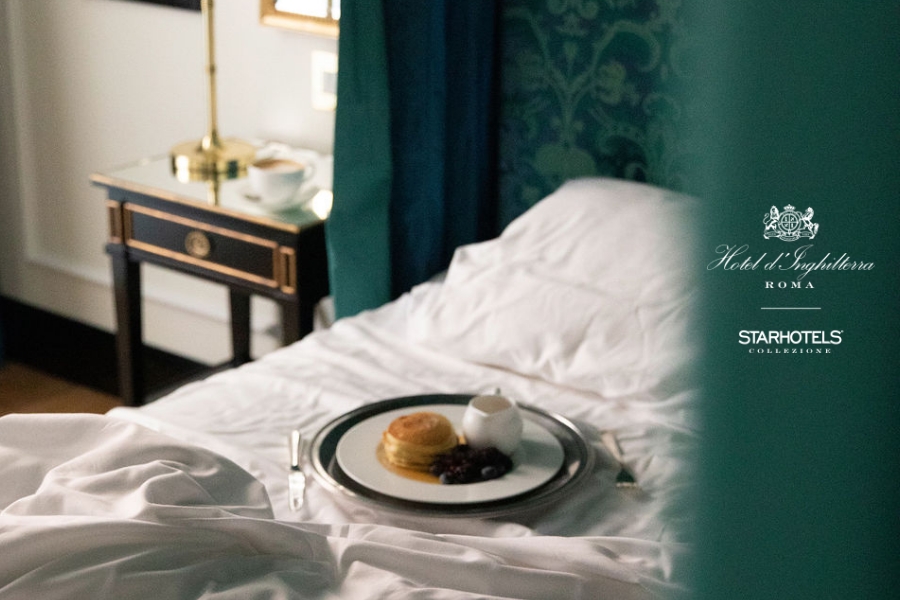 A breakfast tray with pancakes, syrup, and berries sits on a white bed; Hotel d’Inghilterra Roma logo appears on the right.