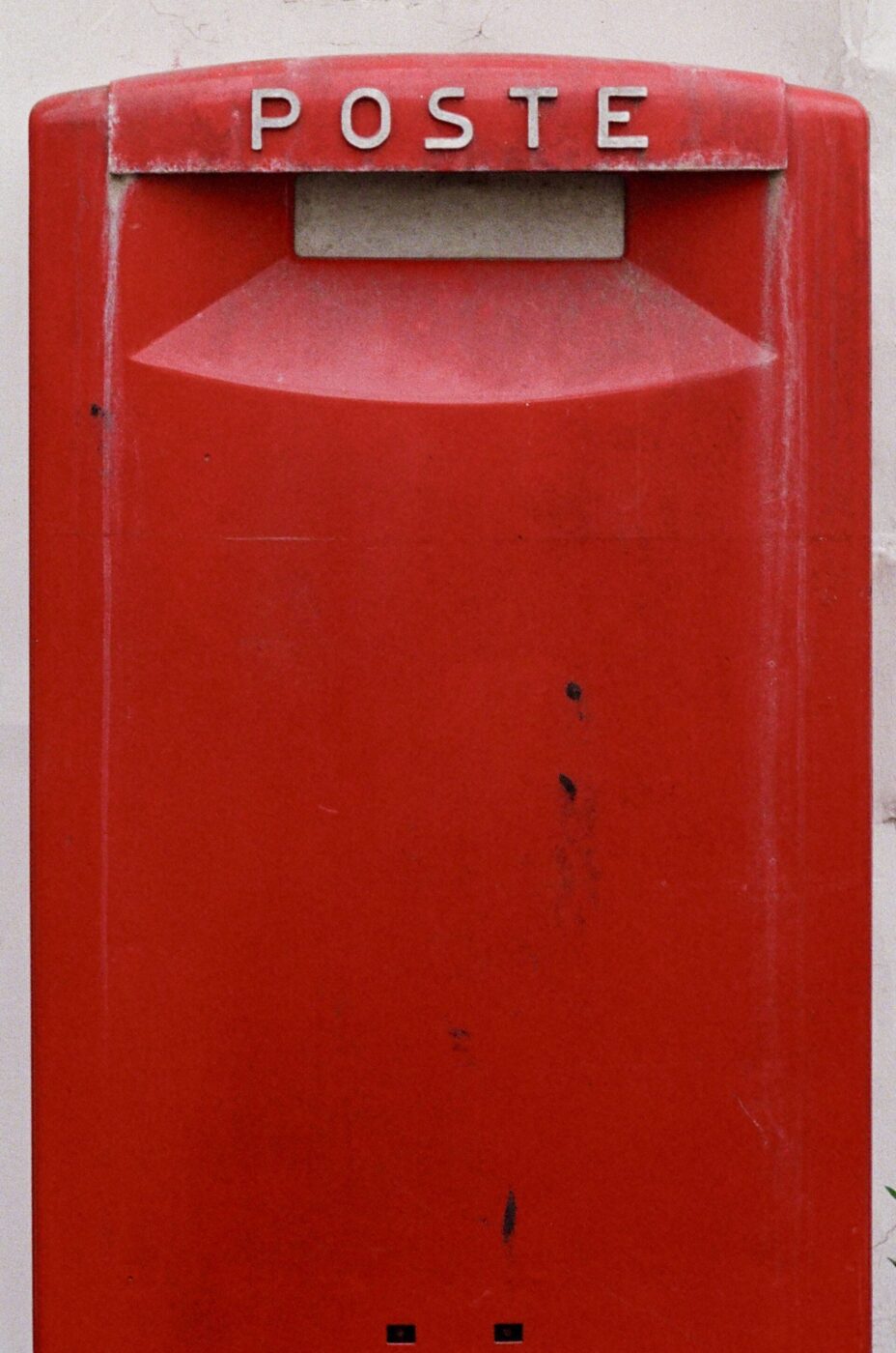 Primo piano di una cassetta postale rossa con l'etichetta POSTE in bianco, su uno sfondo semplice. La cassetta presenta segni di usura e di utilizzo.